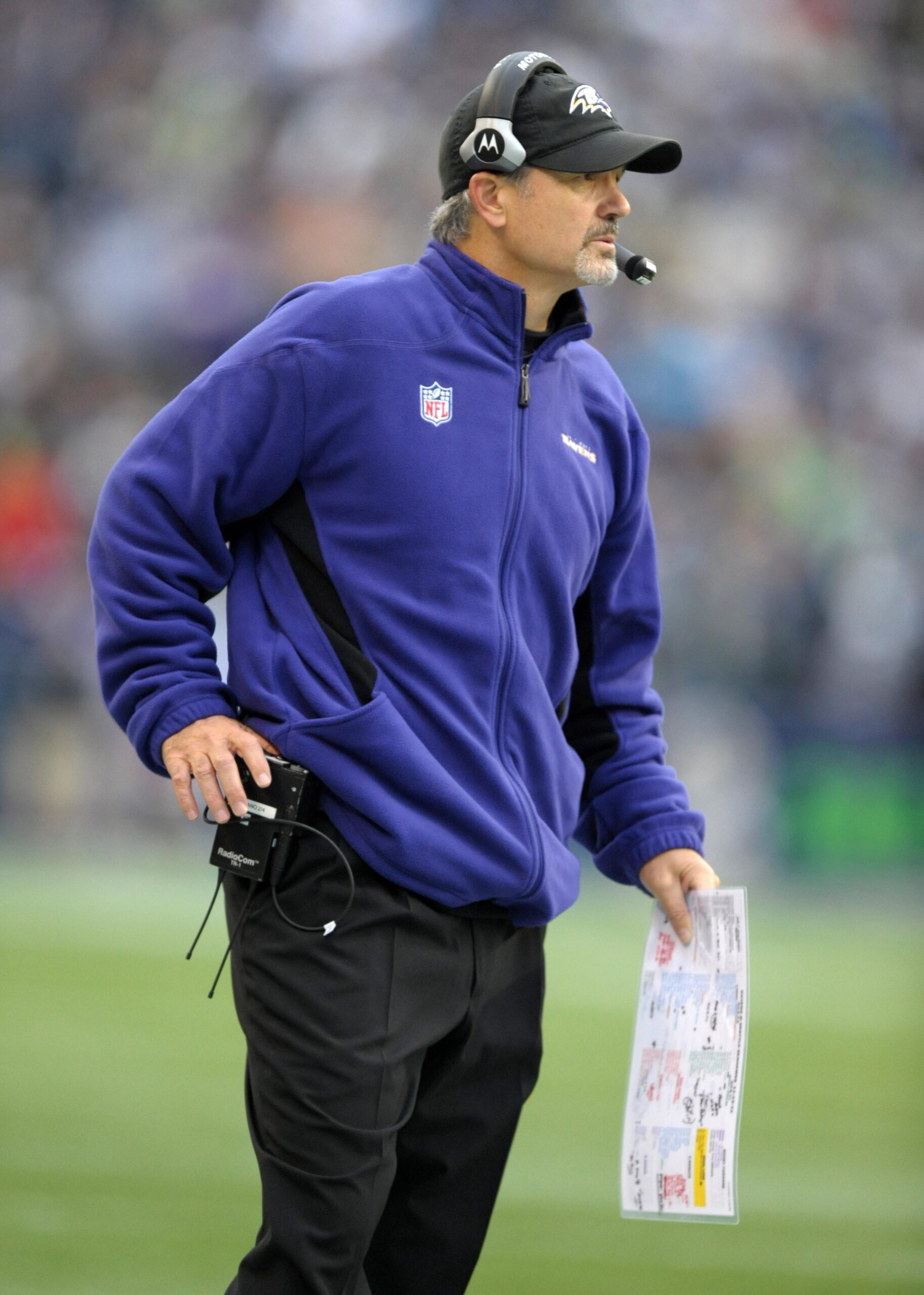 A coach on the sideline in a headset, holding a play sheet.